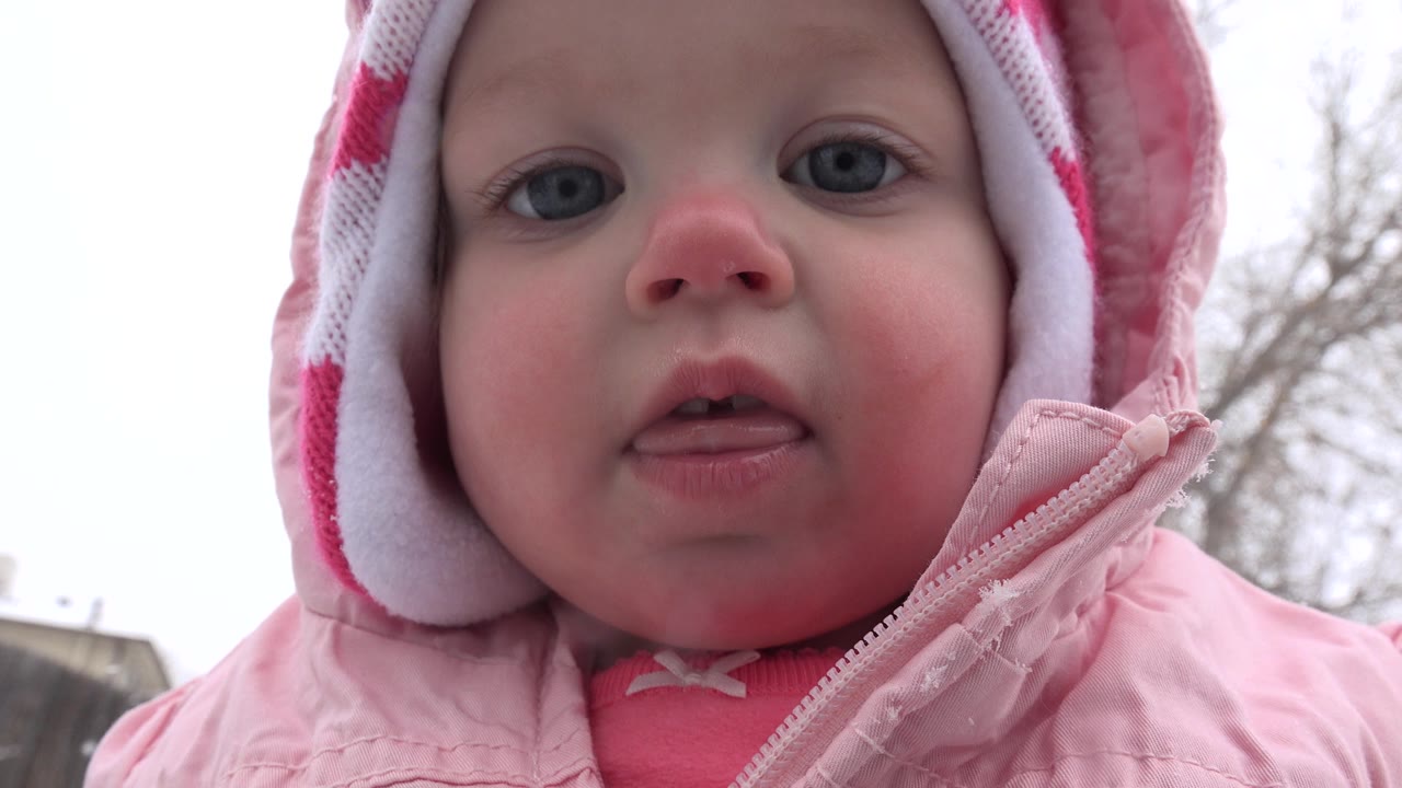 Close-up of a bundled child in a pink winter coat and red knit hat.