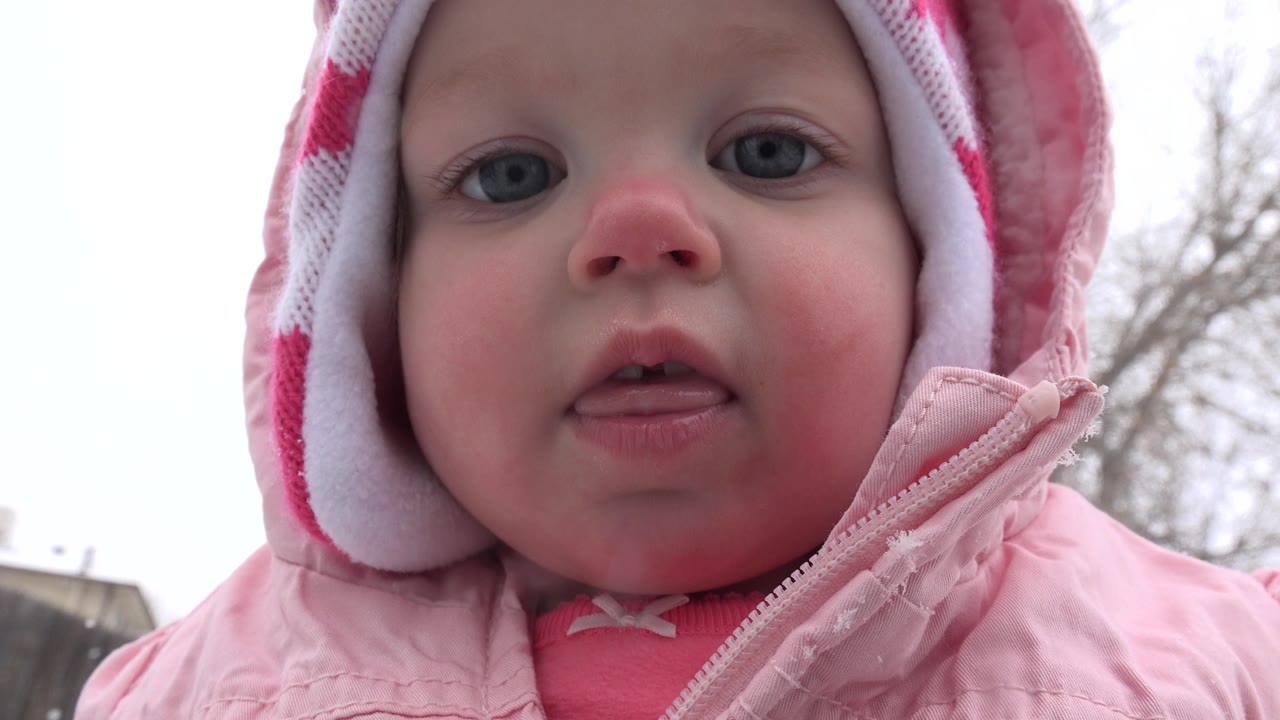 The child remains close to camera in Westminster, Colorado, looking forward in a pink coat and patterned red hat against a pale winter sky.