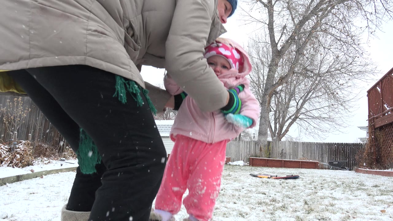The Westminster backyard view is partly blocked by the woman's tan coat as she lifts the baby in pink closer to her body.