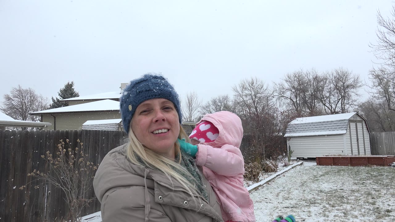 In Westminster, Colorado, the woman faces the camera while holding the child in pink, with a shed and snow-dusted lawn visible behind them.