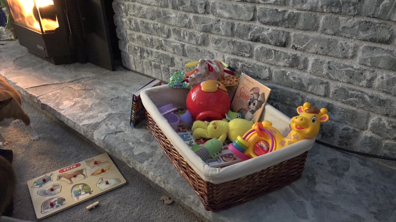 Basket of colorful toys beside a book on a gray stone hearth near a fireplace.