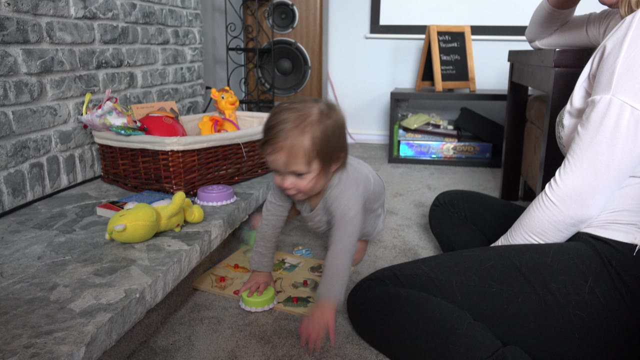 Toddler crouches by scattered toys near a living room fireplace.