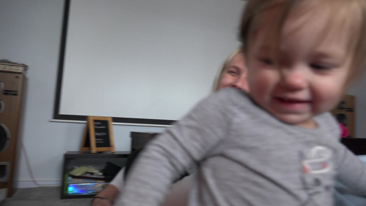 In Westminster, Colorado, the baby remains in soft focus near the lens with a small smile, while the seated woman is partly visible behind her.