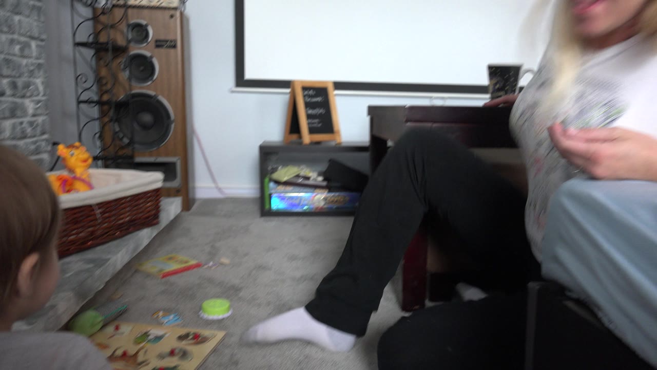 Toddler near toys on a carpeted living room floor with an adult partly visible.