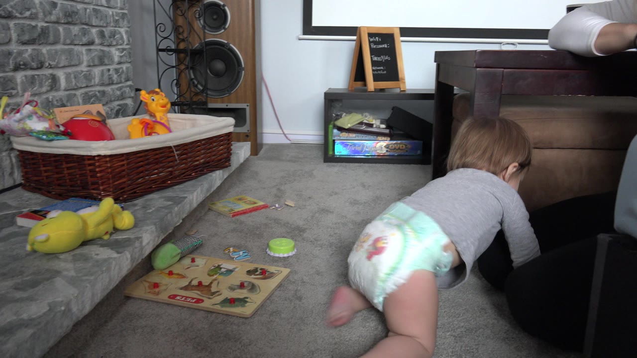 Toddler crawling on carpet toward furniture near scattered toys.