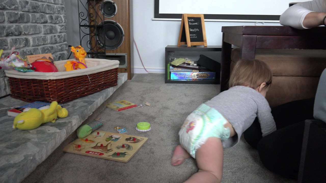 The toddler remains low on the carpet in the Westminster, Colorado interior, crawling beside a puzzle board and scattered toys while the play basket sits against a stone-textured wall.