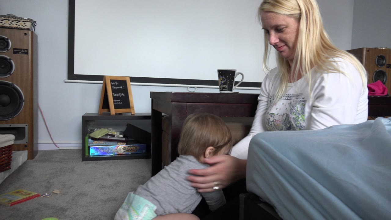 In Westminster, Colorado, the woman places her hands around the baby as the child leans forward near the table and blue blanket in the living room.
