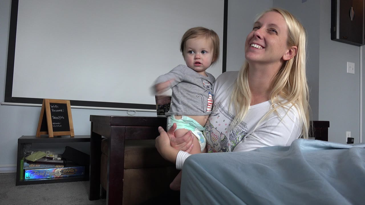 Mother holding a baby as the child looks sideways indoors.