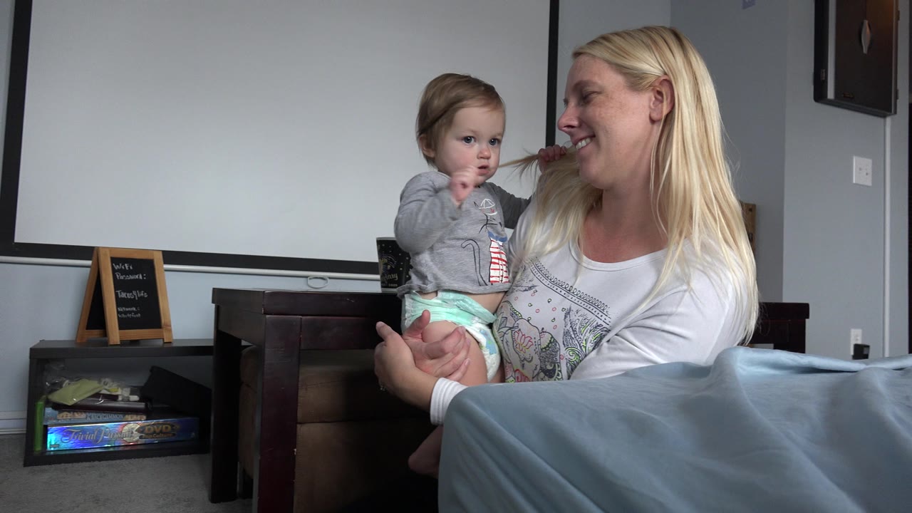 Blonde woman holds a young child indoors as the child touches her hair.