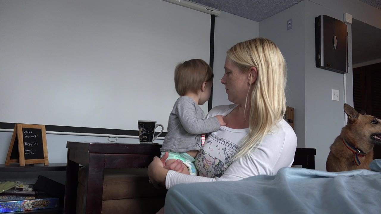 In Westminster, Colorado, the woman keeps the child on her hip as they face each other, with the tan dog, chalkboard sign, and dark furniture visible behind them.