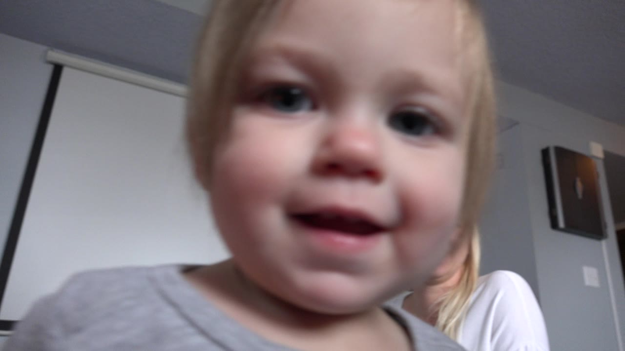 Toddler centered close to camera with woman obscured in the background.