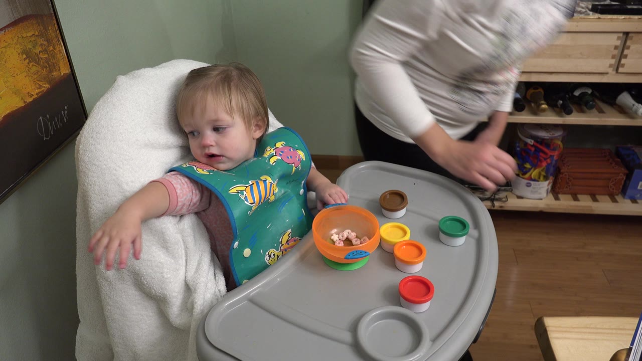 Baby in a high chair beside an adult during mealtime.