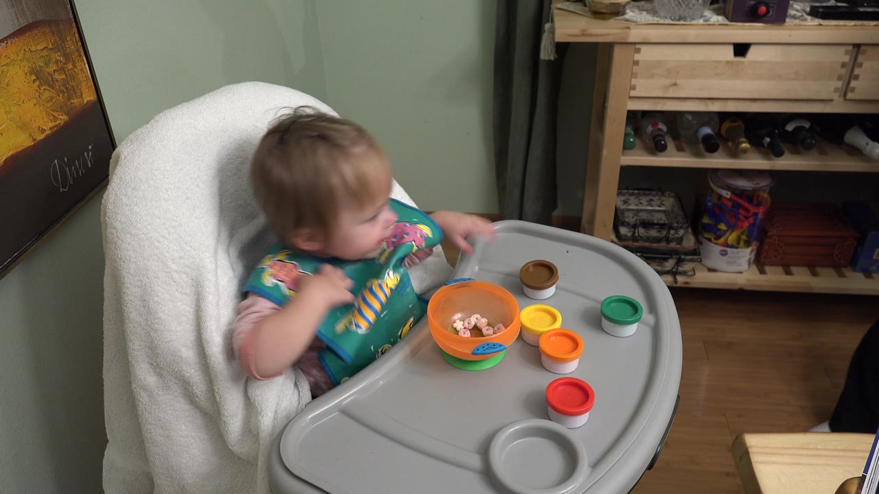 Baby in a high chair with a bowl and colorful lids on the tray.