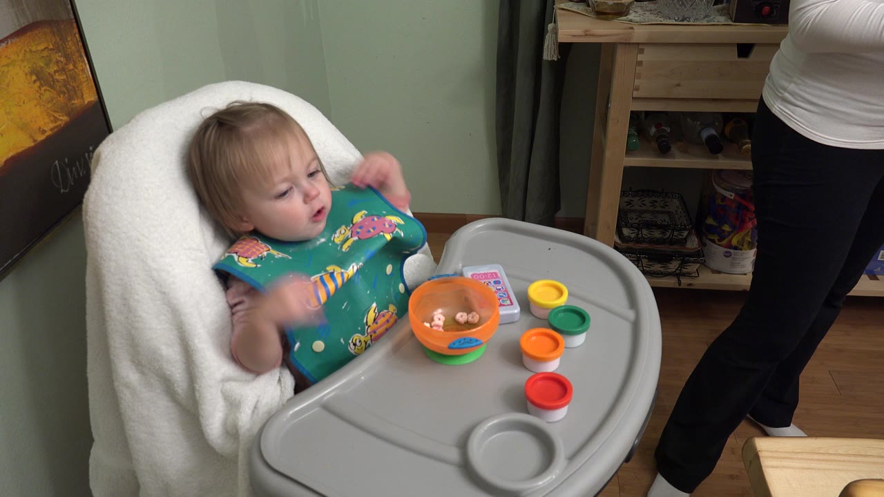 Baby in high chair with bowl and colored cups on tray