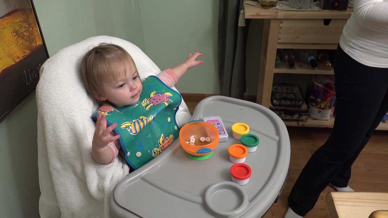 Baby in a high chair reaching beside a food tray.
