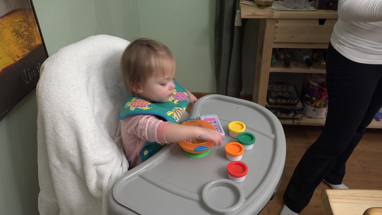 Baby girl in a high chair reaching toward an orange bowl.