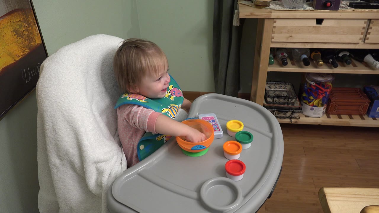 Toddler reaches into a bowl while seated in a high chair.
