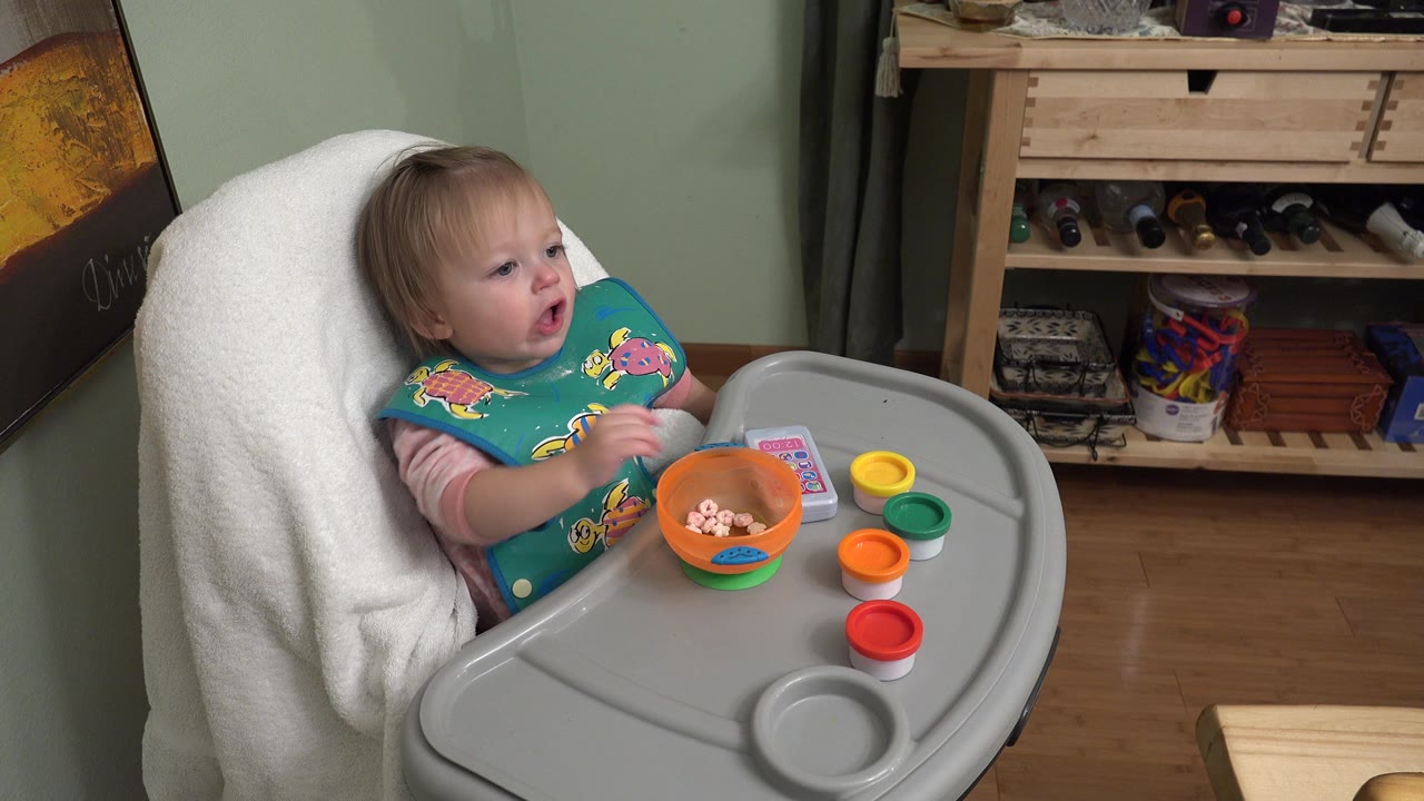Toddler in a high chair with an orange bowl on the tray.