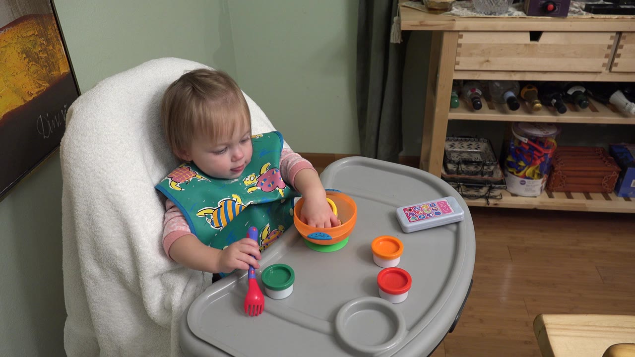 Infant in a high chair reaches toward bowls on the tray.