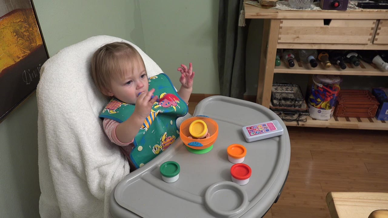 Baby girl in a high chair with colorful cups on the tray.
