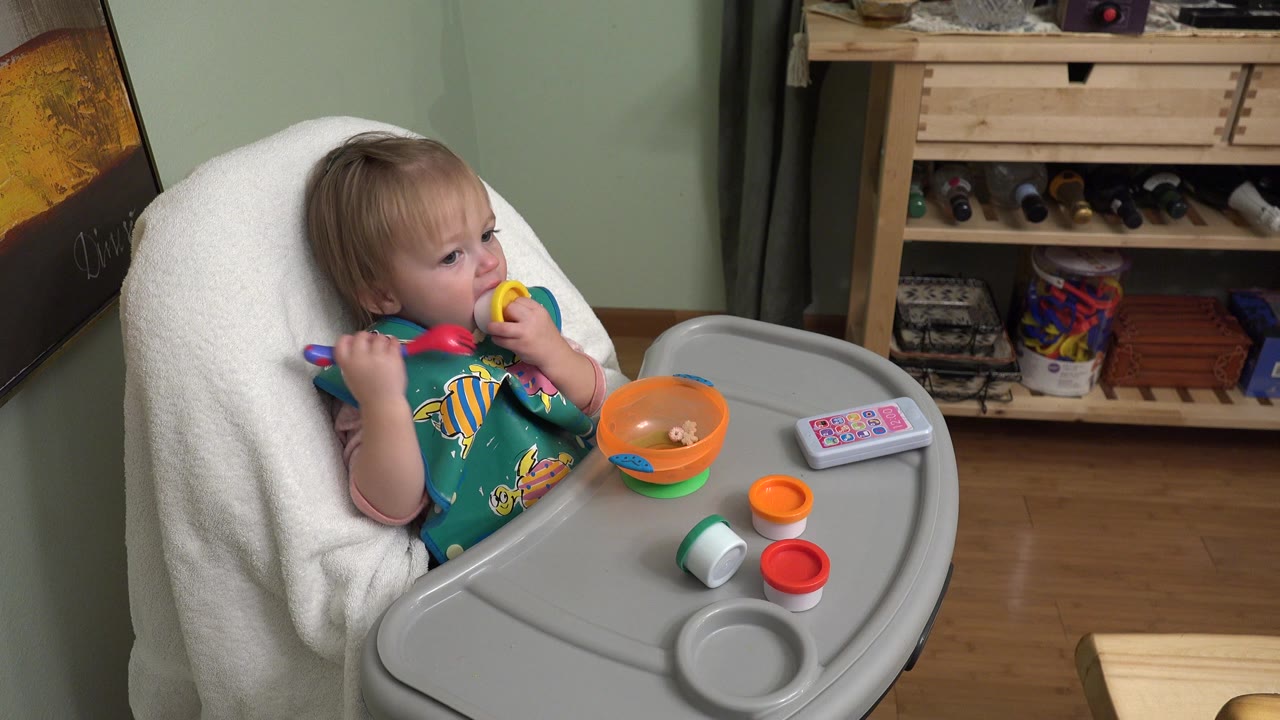 Toddler in a high chair holding colorful toy kitchen pieces.