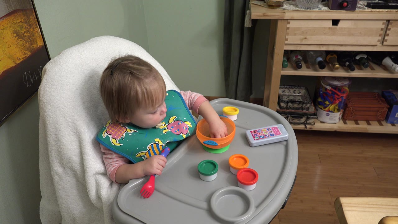 Baby in a high chair reaching into an orange bowl on a tray.