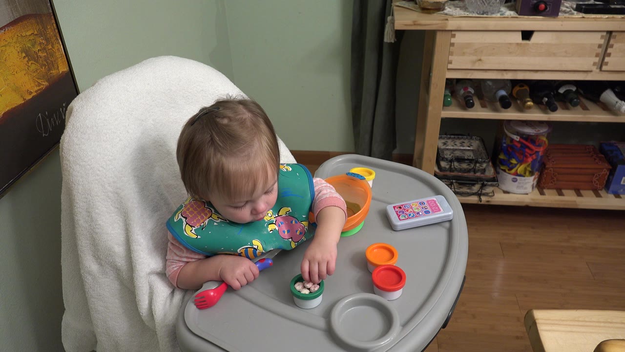 Baby in a high chair looking down at food on a tray.