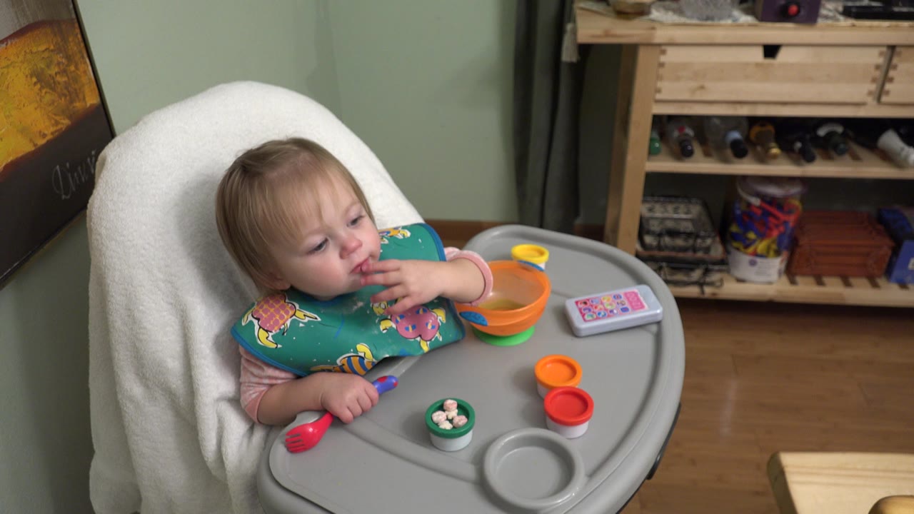 Baby in a high chair with a hand near their mouth and food items on the tray.