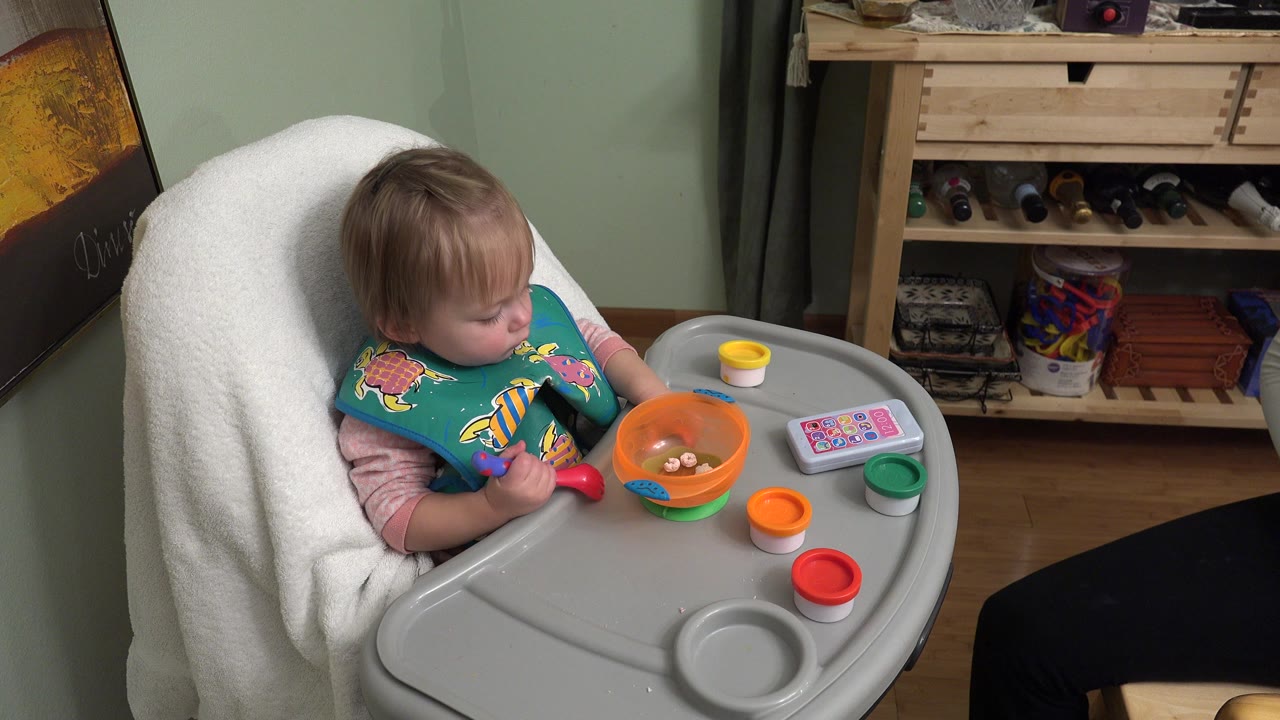 Toddler seated in a high chair with a bowl and spoon on the tray.