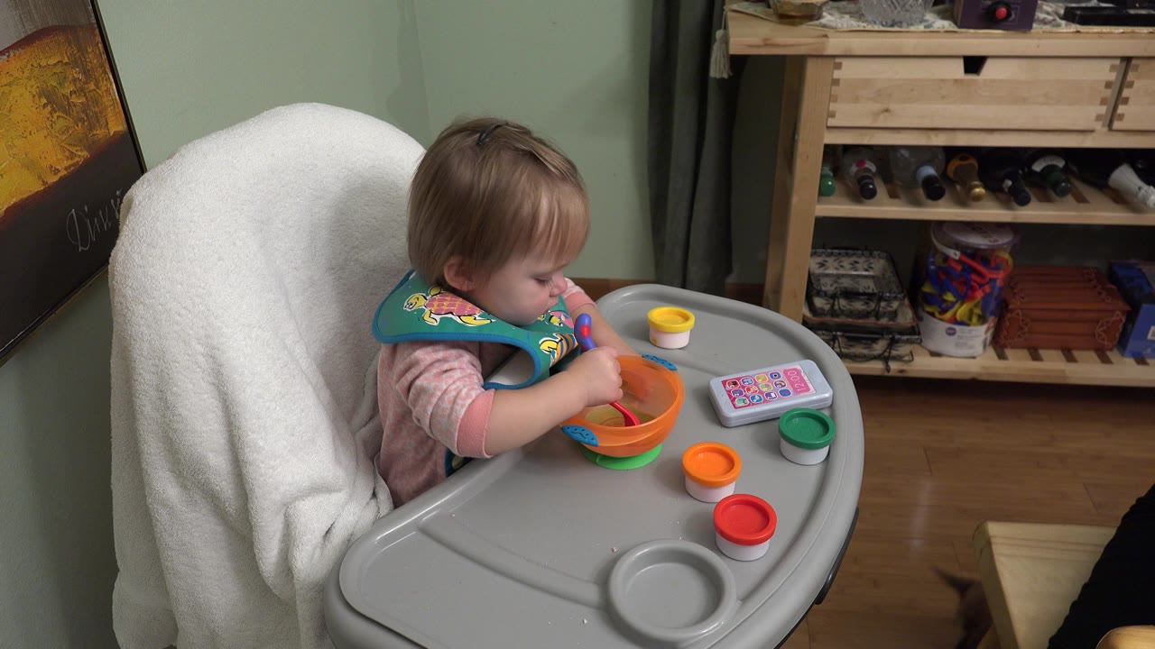Blonde child eating from a bowl in a high chair indoors.