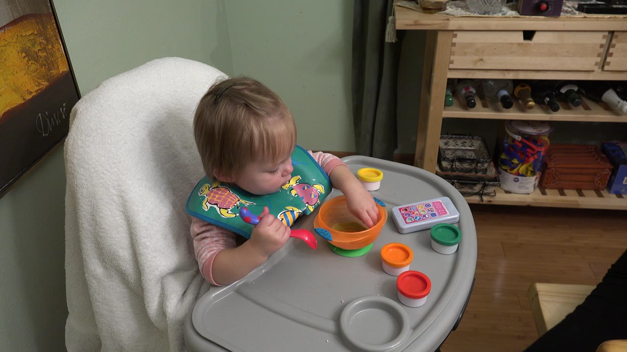 Toddler in a high chair reaching toward toy bowls on a tray.