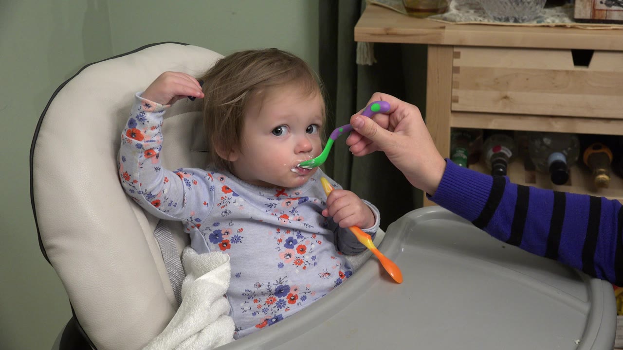 Baby in a high chair being fed with a green spoon.