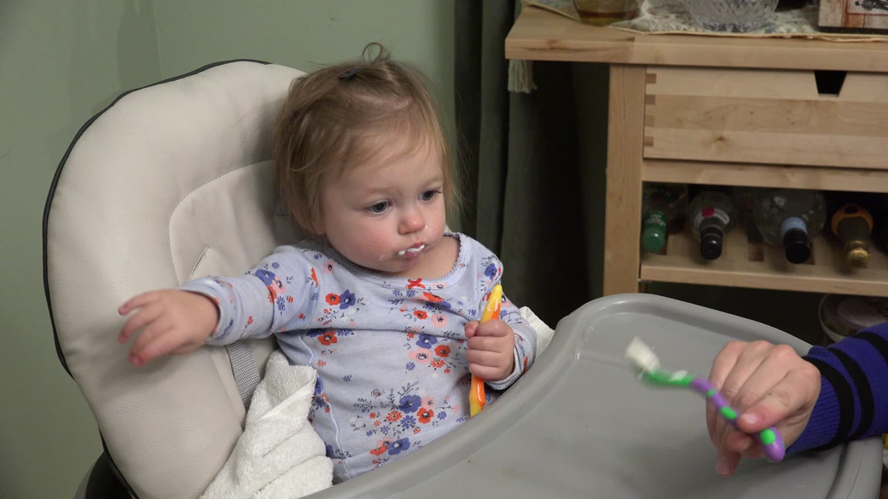 The Westminster, Colorado home scene holds on the toddler with food on their mouth while an adult hand keeps the spoon near the high chair tray.