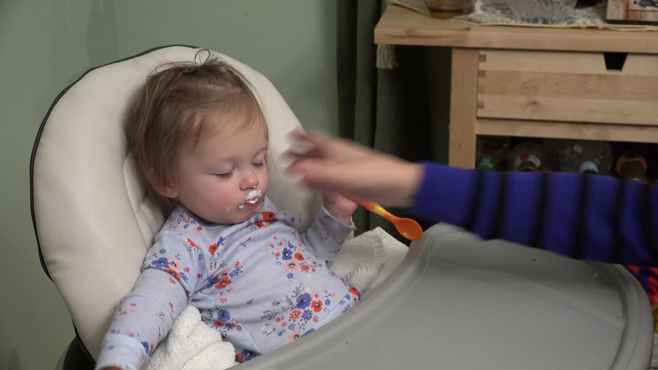 The Westminster, Colorado frame shows the toddler looking down as an adult hand hovers near the child's face beside the high chair tray.