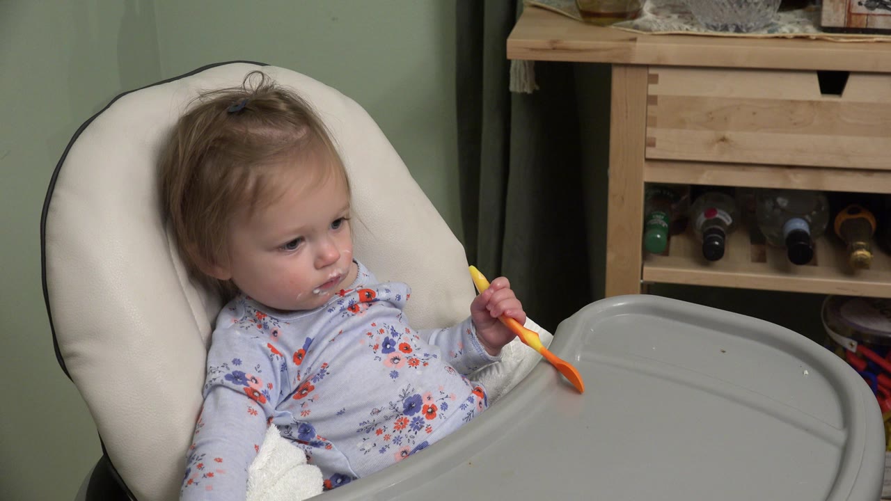 Baby in a highchair holding a spoon beside a gray tray.