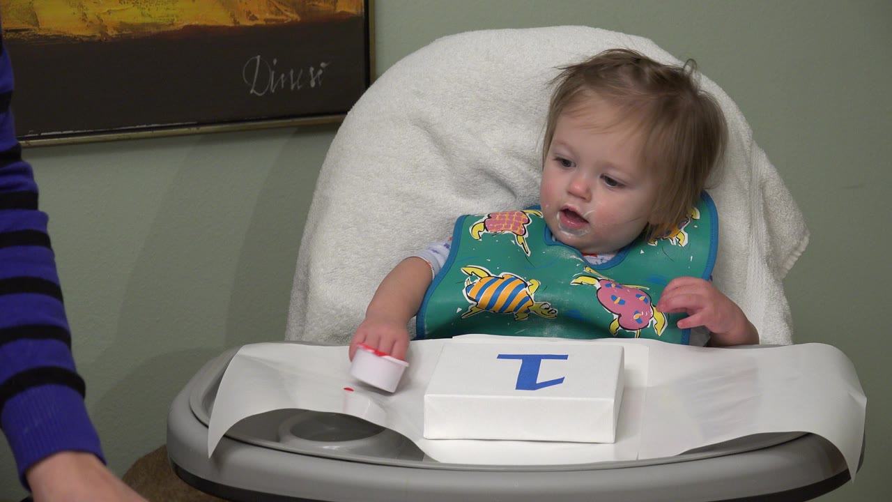 Baby in a high chair touches a small red paint cup.
