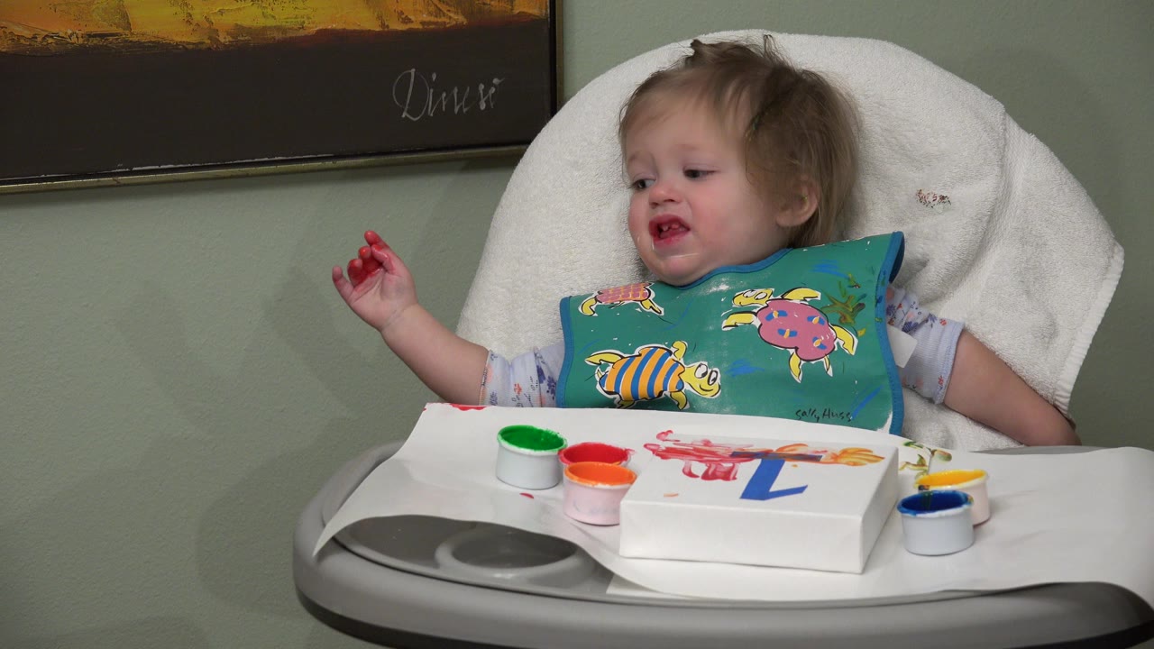 Toddler in a high chair with paint cups and number activity on the tray.