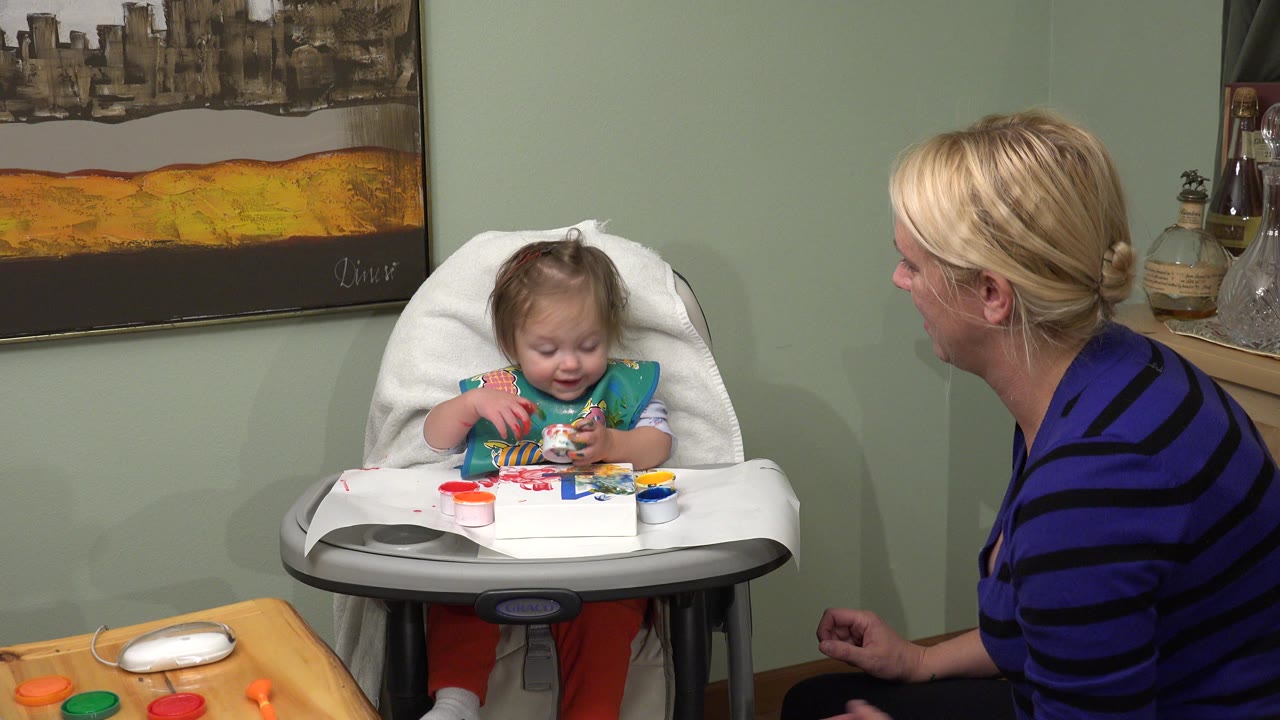 Baby in a high chair with mother seated beside her