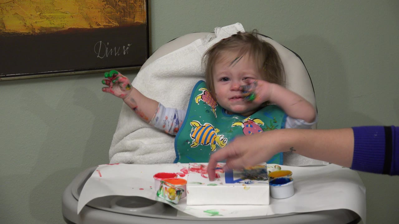 Baby girl in a high chair with paint on her hands and face.