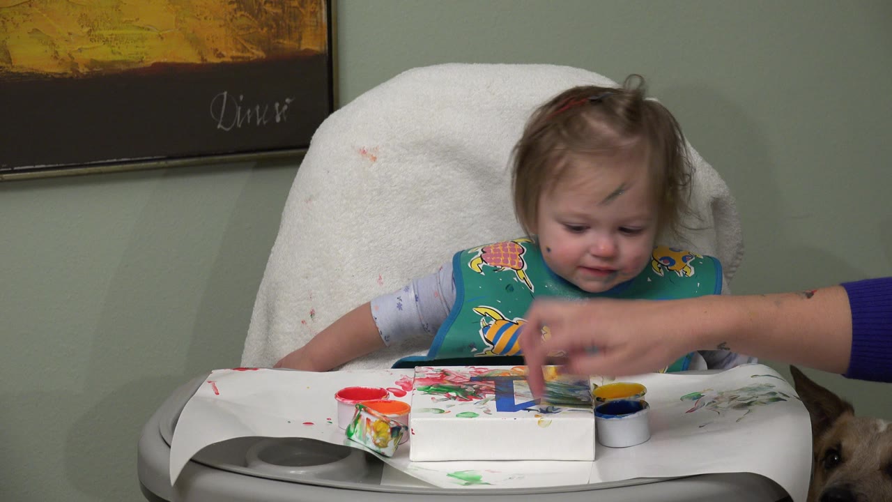 Young child in a highchair with finger paints on the tray.