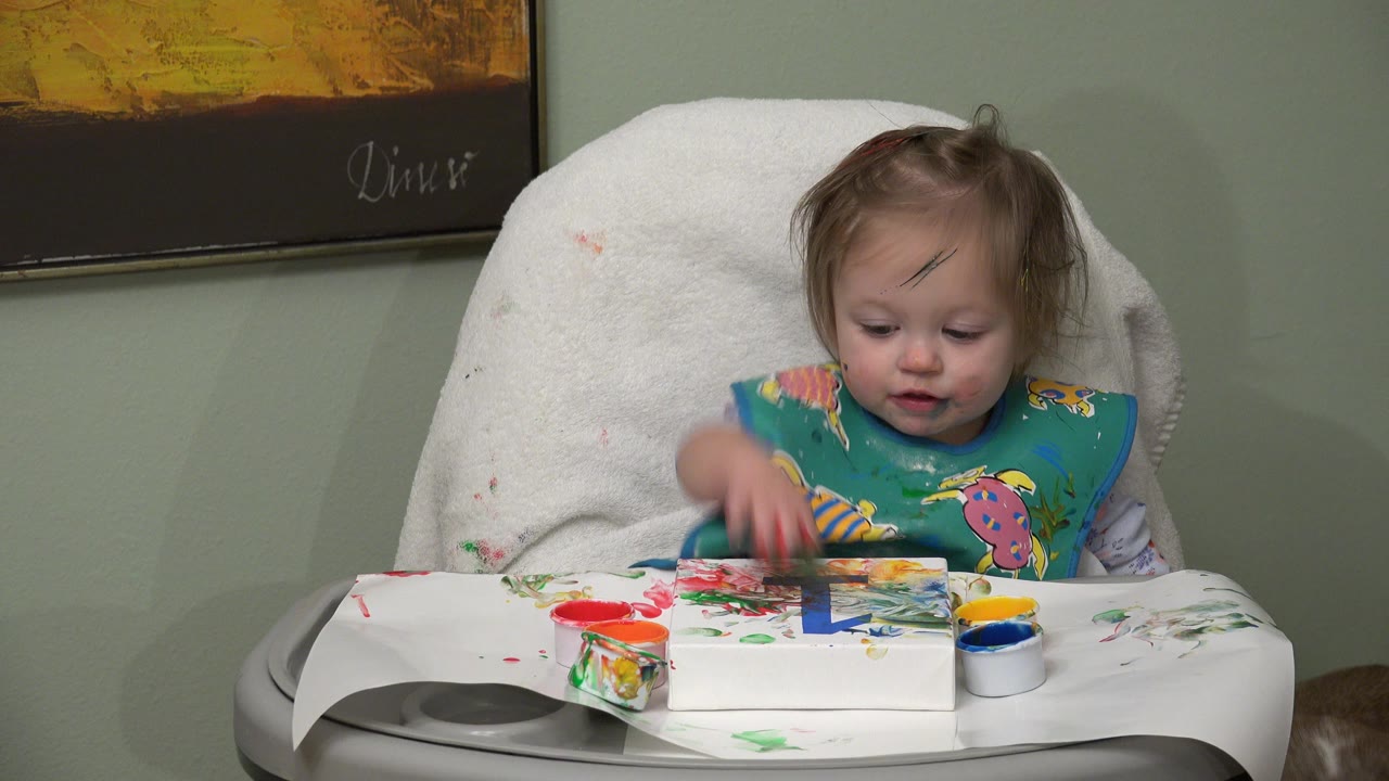 Toddler in a high chair reaching toward paint on a tray.