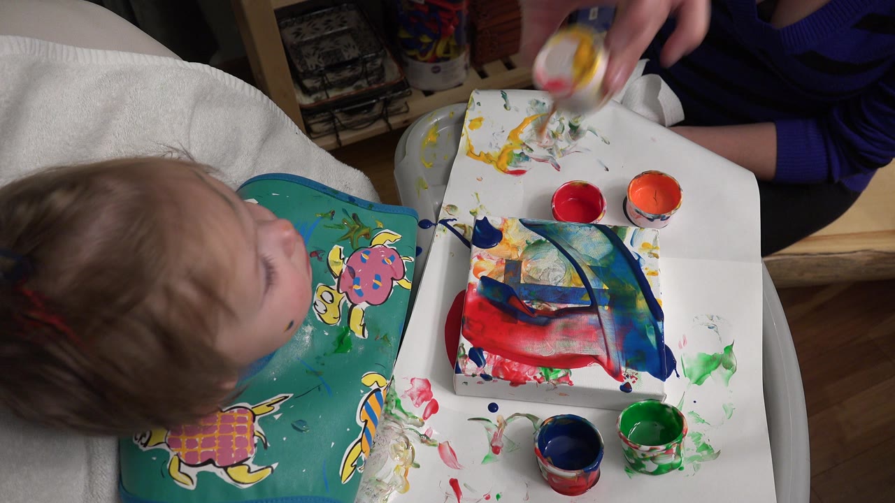 Young child beside a tray covered with colorful paint and paper.