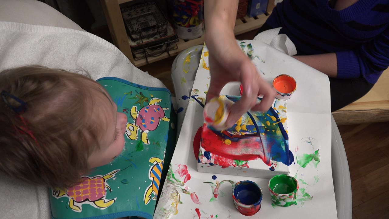 Toddler in a high chair beside paint cups and a painted paper tray.