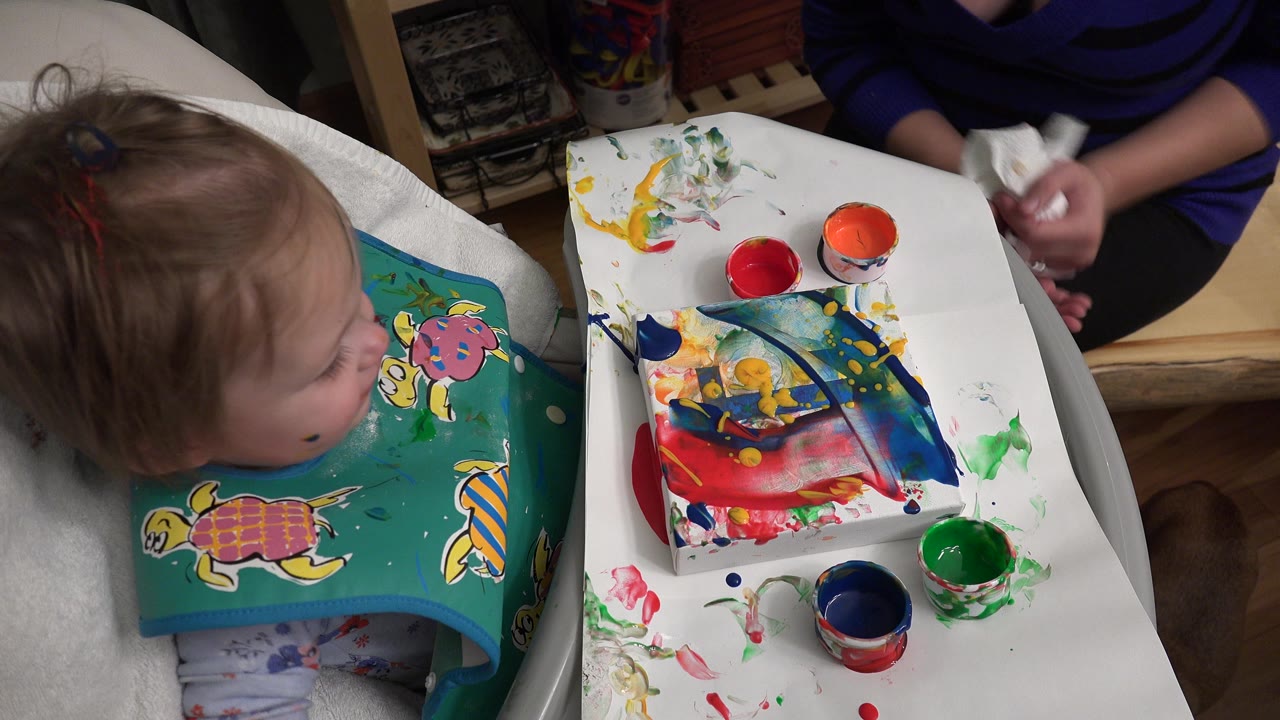 Young child in a high chair beside paint cups and a painted tray.