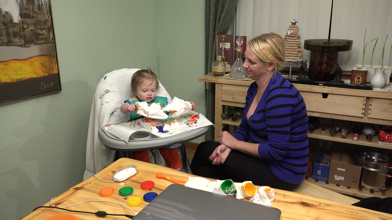 Baby in a highchair beside a seated woman in a home dining room.