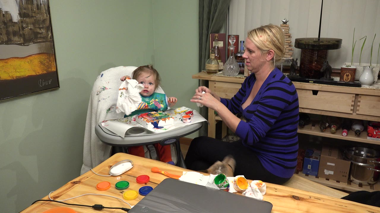 Woman beside toddler in high chair with paper towel in her hands.