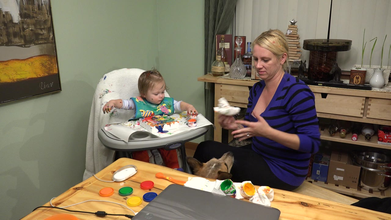 The mother holds a cloth or paper towel beside the high chair as the young girl looks toward the coloring materials in the Westminster, Colorado interior.