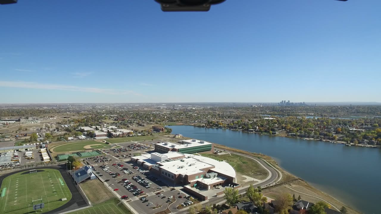 Drone view over athletic fields, a large building, parking lots, and water