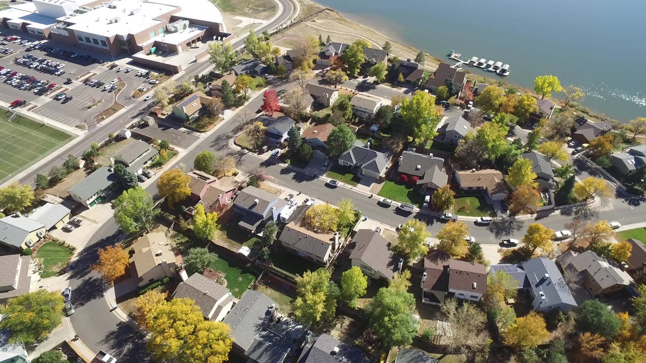 High aerial frame over Hidden Lake, Colorado homes, curving streets, a shoreline, lake water, docks, a large parking lot, and no visible people.