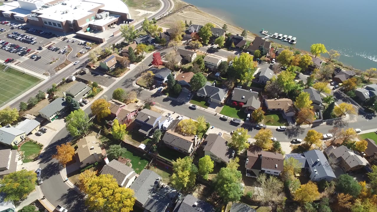 Drone-style view of lakeside neighborhood with homes and colorful trees.